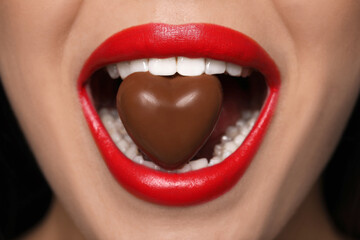Young woman with red lips eating heart shaped chocolate candy, closeup