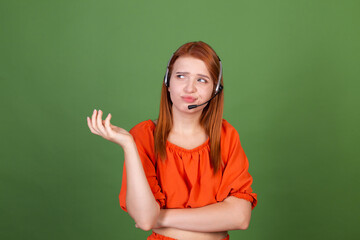 Young red hair woman in casual orange blouse on green background manager call centre help line worker with headphones talk tired exhausted