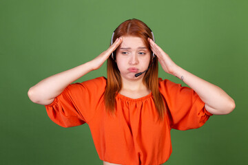 Young red hair woman in casual orange blouse on green background manager call centre help line worker with headphones talk tired exhausted