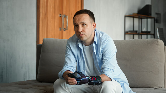 Interested bald guy with artificial hand prothesis switches television channels with remote controller