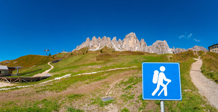Panoramic view of magical Dolomite peaks of Pizes da Cir, Passo Gardena at blue sky and sunny day with a post sign trailhead showing a walking man, hiker at the tral , South Tyrol, Italy.