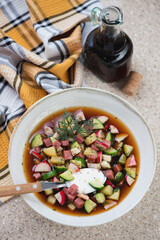 Plate of okroshka or russian traditional cold soup with kvass, vertical shot on a beige marble background, elevated view