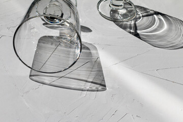 Glass on a grey concrete table with sunbeams and reflections, view from above, abstract shadows and sunlight
