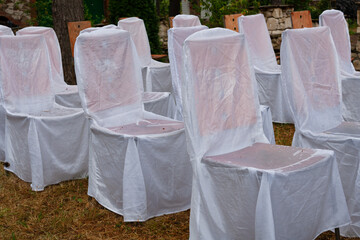 Wooden chairs in white covers for a celebration after the rain in a country estate.