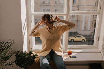 Chilling young brunette listening music. Attractive short-haired girl with white headphones,...