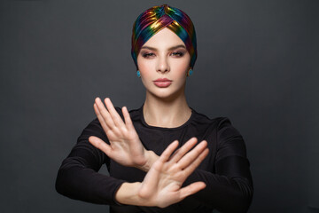 Confident woman in turban showing stop gesture and saying no on black background
