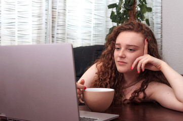 Fototapeta premium Portrait of young redhead with serious face looking at her computer screen.