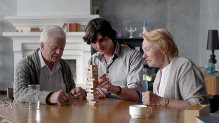 Happy grandparents and young grandson play board game at home