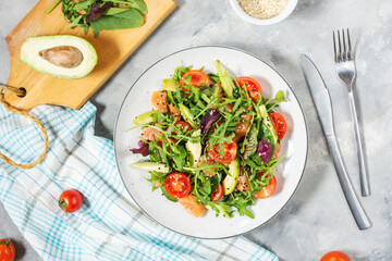 Salmon salad with green leaves, avocado and cherry tomato on concrete background.