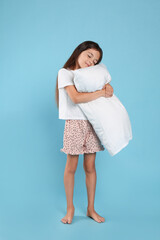 Cute girl wearing pajamas with pillow on light blue background