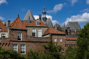 Naklejka premium Medieval city wall of Hanseatic city Zutphen in The Netherlands against a blue sky with cumulus clouds in full sunlight with greenery in front. Historic architectural detail of Dutch town.