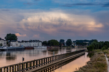 Vibrant sunset colors reflecting cityscape countenance of Zutphen in The Netherlands with large cumulonimbus rain cloud rising above river IJssel tower town. Dutch weather condition landscape.