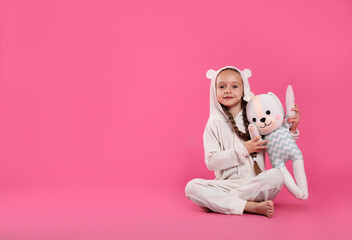 Cute girl wearing pajamas with toy on pink background. Space for text