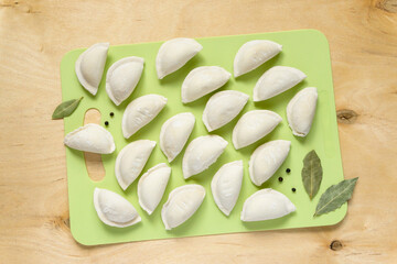 Raw frozen dumplings with bay leaf and pepper on cutting board, top view