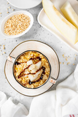 Millet porridge with melon slices and walnuts in a ceramic bowl on a light gray kitchen table top view. Delicious and healthy breakfast	
