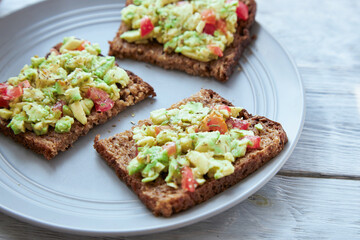 Vegetarian green sandwiches with avocado and tomatoes chopped on wooden grey table