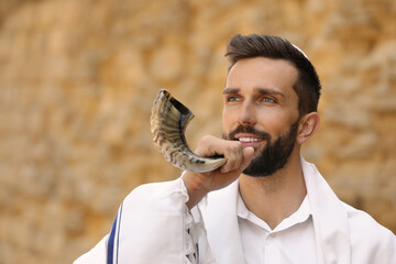 Jewish man in kippah and tallit blowing shofar outdoors. Rosh Hashanah celebration