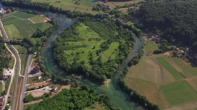 Aerial view of river deviation and island with roads, houses and fields surrounding.