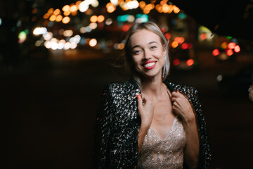 Beautiful blonde woman smiling looking at camera outdoors at night city lights street. Stylish...