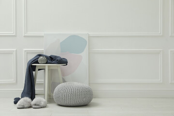 Knitted pouf, fuzzy slippers and decor elements near white wall indoors. Space for text
