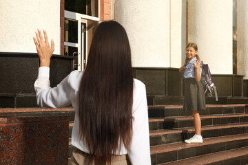 Mother waving goodbye to her daughter near school entrance