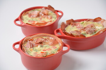 Proсess of cooking Omelette  with bacon, grated parmesan and greens. Raw beaten egg yolks  with ingredients in ceramic cocotte