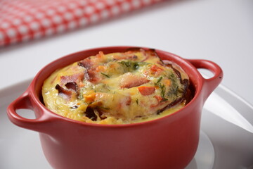 Omelette  with bacon, grated parmesan and greens in ceramic cocotte. Tasty breakfast