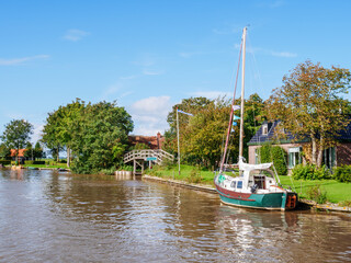 Fototapeta na wymiar Dokkumer Ee canal with sailboat and bridge in Burdaard in Friesland, Netherlands