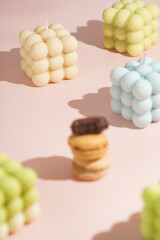 Three creamy, pink and chocolate macaron pastry stacked on top of each other surrounded by bright bubble candles on pink surface