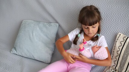 Cute charming adorable little female child sitting on sofa in living room taking her favorite doll to bed, kid wearing white t shirt and pink short.