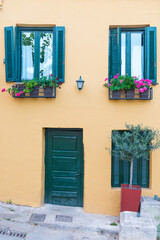 Windows with blue shutters on the white wall and blooming pink flowers