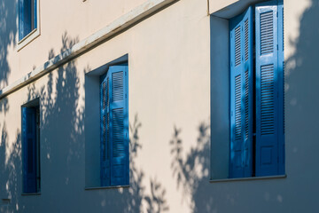 Windows with blue shutters on the white wall in greek style