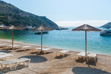 Summer vacation destination. Straw sunshades and sunbeds on the empty  beach with sea in the background.