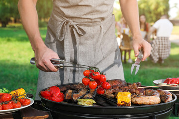 Man cooking meat and vegetables on barbecue grill outdoors, closeup