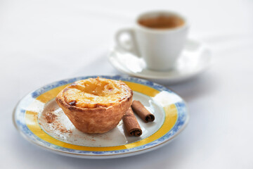 Pastel de Belem em primeiro plano com xícara de café desfocada ao fundo