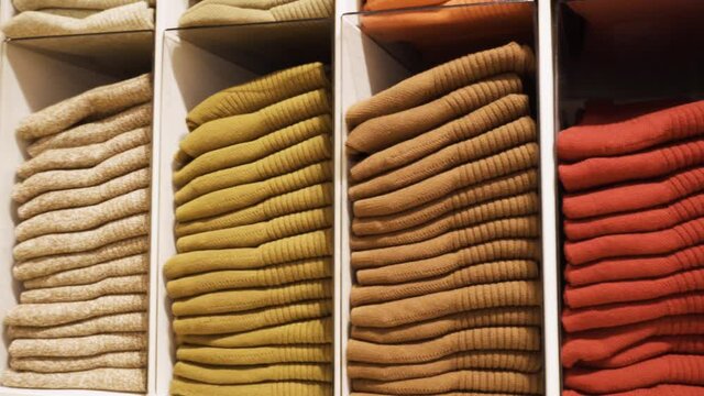 Lots of new socks on the shelf in a clothing store. A row of multi-colored stacks in the store. Inside the store. Close-up. Shopping. Pan shot.