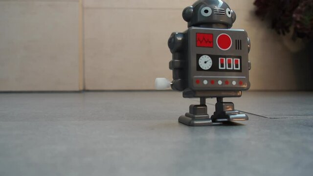 Retro toy robot walking towards camera. Mechanic plastic robot with key for turning on. Vintage Toy for children and playful gift. Close up of moving little toy robot.