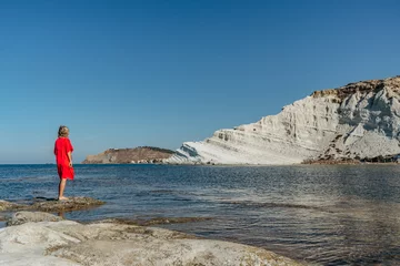 Photo sur Plexiglas Scala dei Turchi, Sicile Scala dei Turchi, Sicile, Italie.Joyeuse femme en robe rouge debout sur la plage, profitant d& 39 une journée d& 39 été ensoleillée.Vue sur les falaises rocheuses blanches, eau claire turquoise.Paysage de vacances de voyage.Fille en vacances