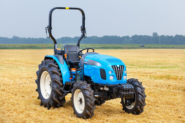 A light farm tractor with a harvested yellow wheat field and a gray, slightly rainy sky in the...