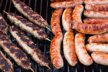 Sausages and minced meat on wooden sticks are cooked on the grill.