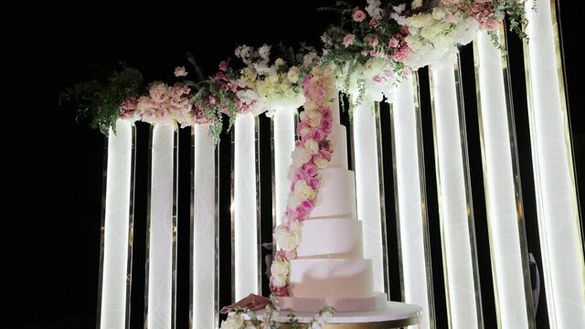 Wedding cake with flowers on the table. White fruit wedding cake on a wedding party night. Wedding arch with flowers on wedding day.