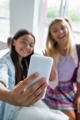 Smartphone in hand of schoolboy taking selfie near blurred friends