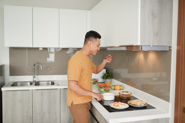 Happy man cooking delicious and healthy food in the loft kitchen at home on sunny day