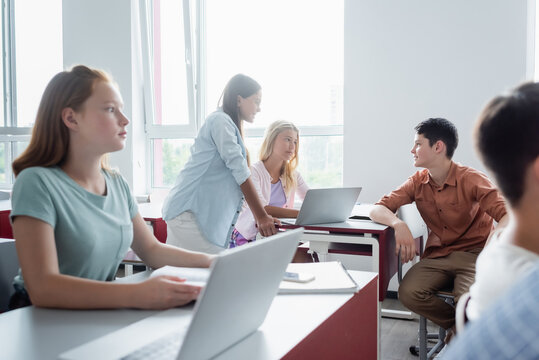 Schoolkids Talking Near Devices And Blurred Friends In Classroom