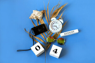 Calendar for August 4 : the name of the month of August in English, cubes with the numbers 0 and 4, a dry palm leaf, a shell, a camera, a watch, sunglasses on a blue background, a top view