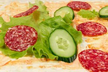 sliced fresh vegetables lie on thin pita bread with ketchup and mayonnaise sauce. salami sausage, cucumber and lettuce. close-up