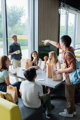 teenage girl pointing at classmate near pupils having lunch in dining room