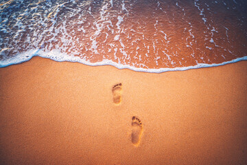 Beach, wave and footprints in sand at sunset time. Tropical island.