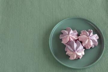 Three colored meringues on a plate, top view, green-blue background