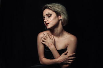 Fototapeta premium Portrait of a girl on a black background. A girl with smeared makeup hugs herself.